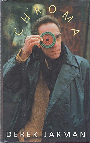 Cover of CHROMA by Derek Jarman. Jarman stands outside in a dark rain jacket, holding a colorful disc over one eye