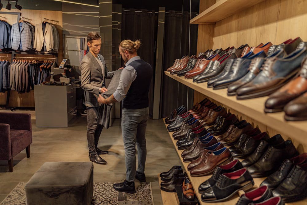 A sales assistant in a gentleman's outfitters helping a customer pick some trousers A sales assistant in a gentleman's outfitters helping a customer pick some trousers