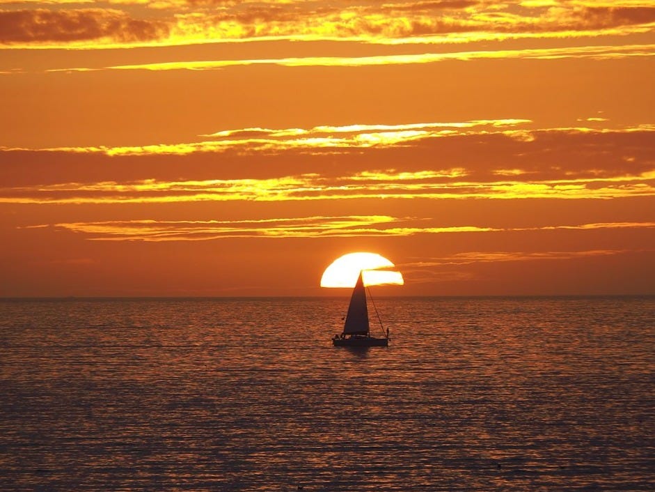 silhouette of person holding umbrella on sea during sunset