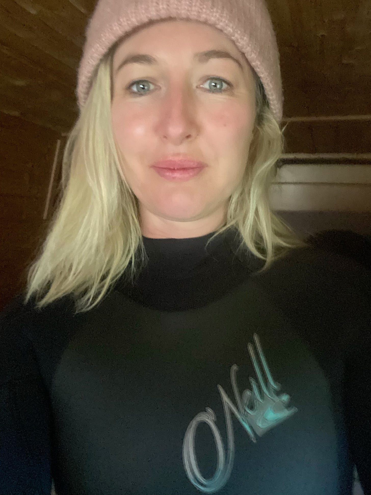 Close of up Sarah Middleton who has long blonde hair, blue eyes and is wearing a black wetsuit and a pink wooly hat