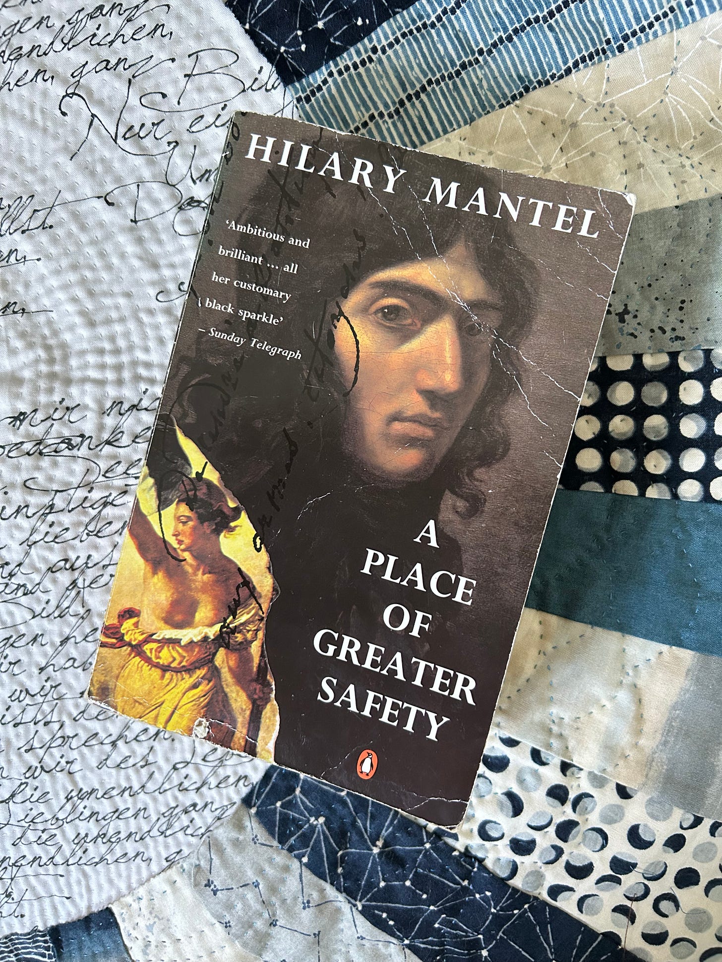 A paperback copy of Hilary Mantel’s A Place of Greater Safety, lying on a quilted piece of fabric