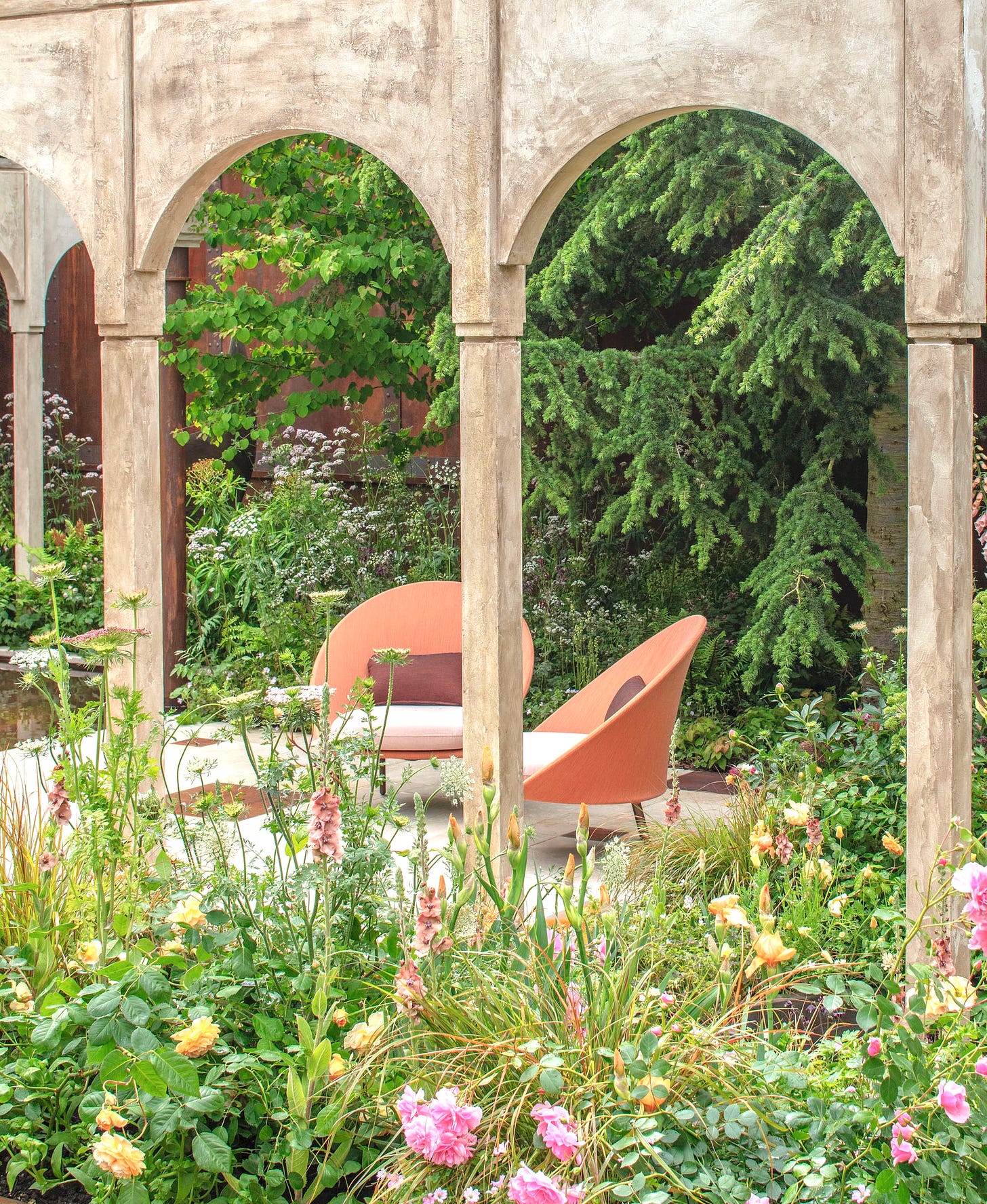 Chelsea flower show garden with arched structure and two orange chairs amongst pretty cottage planting