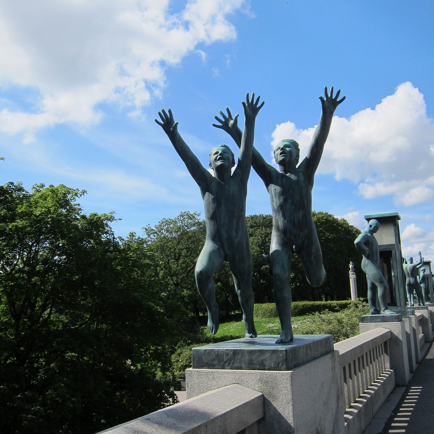 statues of two children running with arms outstretched in front of a blue sky