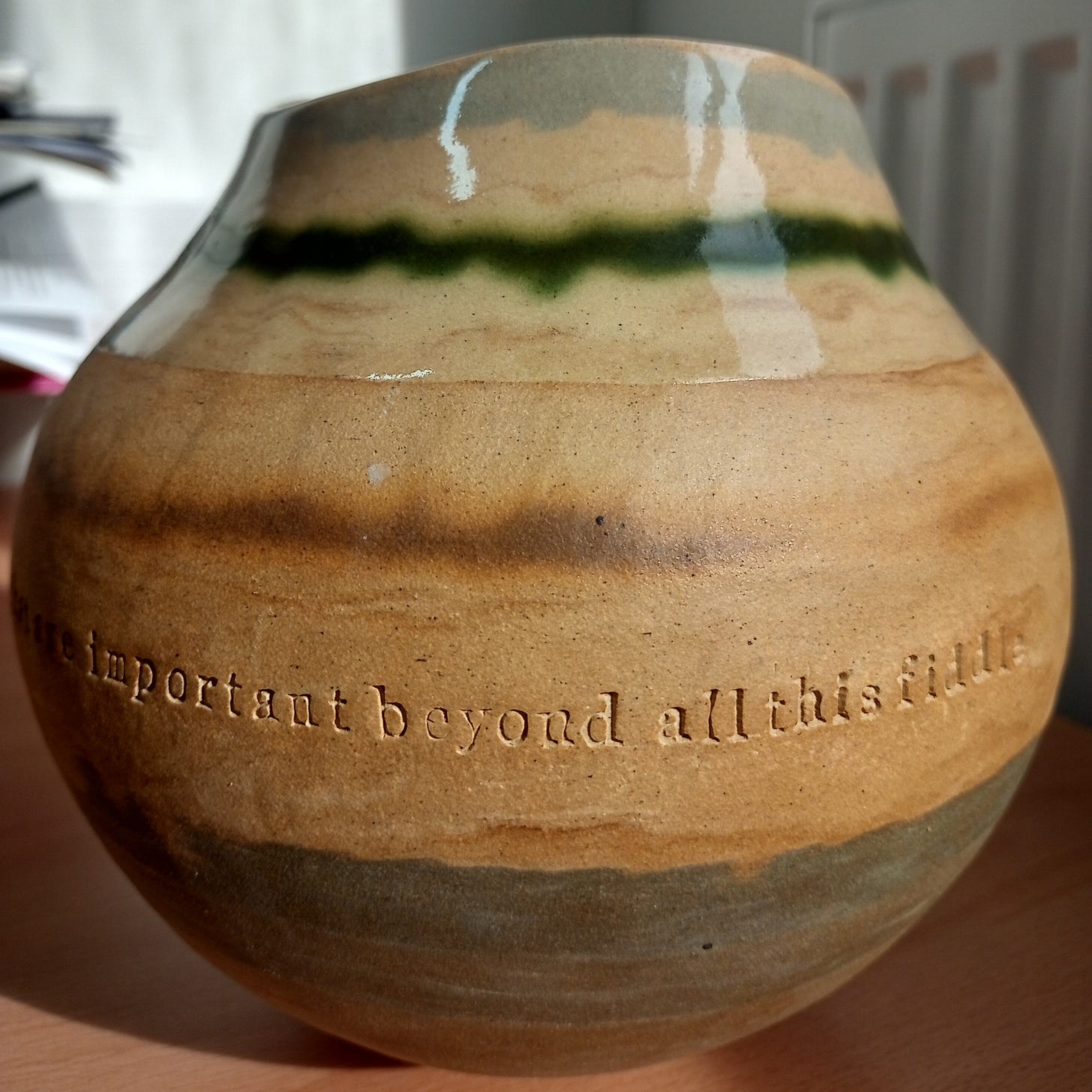 A glazed pot with the words 'important beyond all this fiddle' around its middle