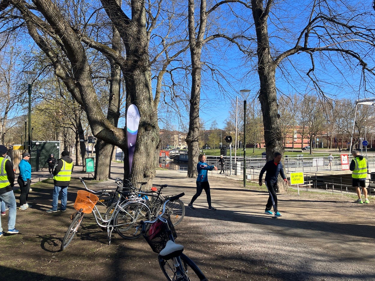 Runners gathering under some trees by the path and bridge