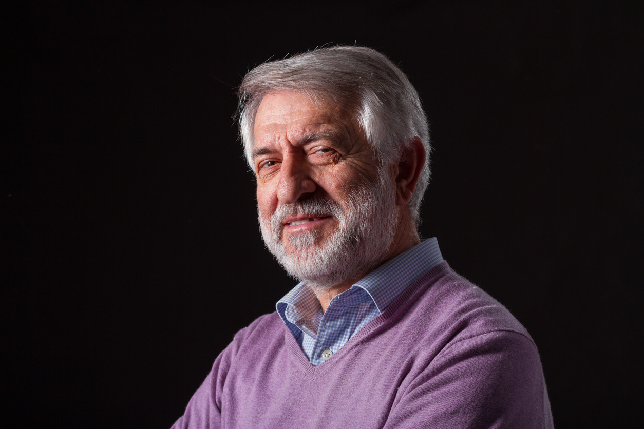 Portrait of elderly white man with a full head of gray hair and short gray mustache and beard smiling as he looks into the camera.