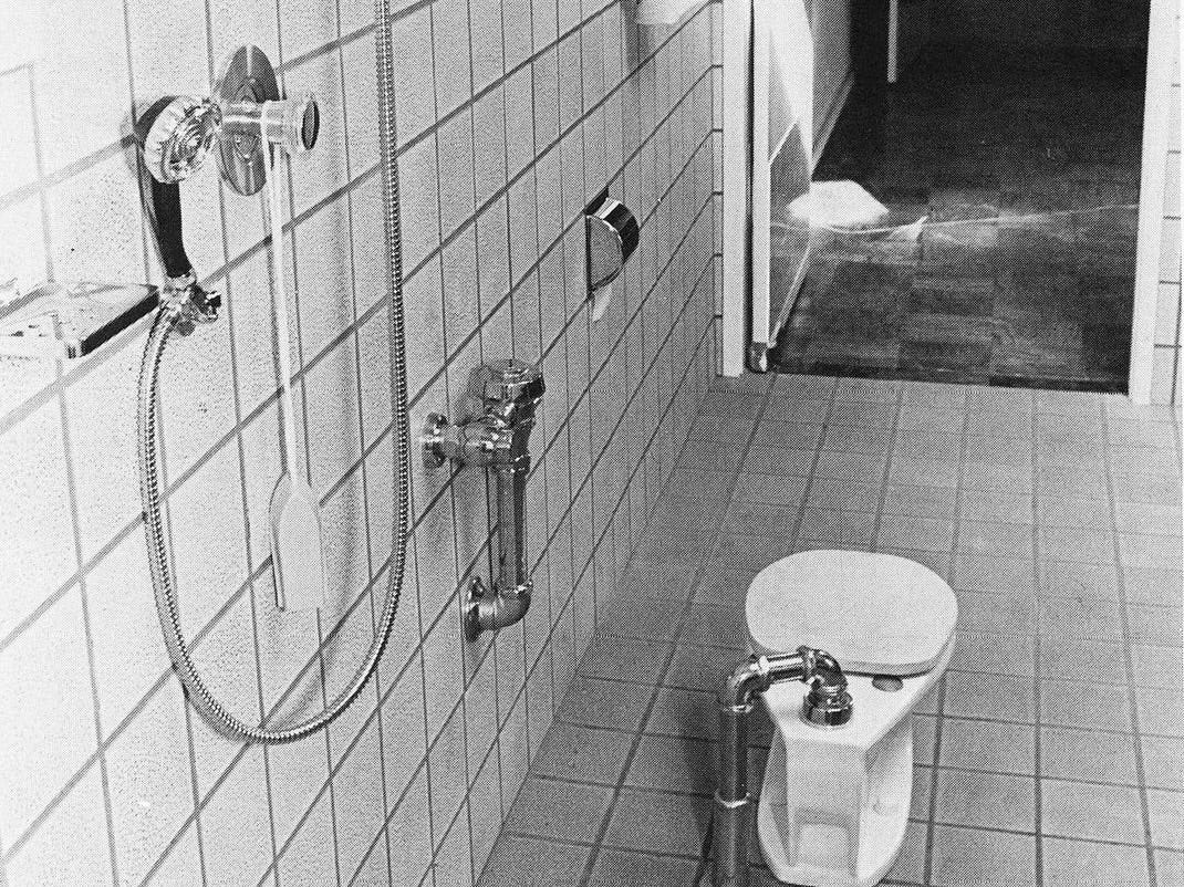 An archival photograph in black and white shows a toilet in Berkeley designed by disabled independent living activists in the 1970s. There’s an unusually slim freestanding toilet in an all-tile room.