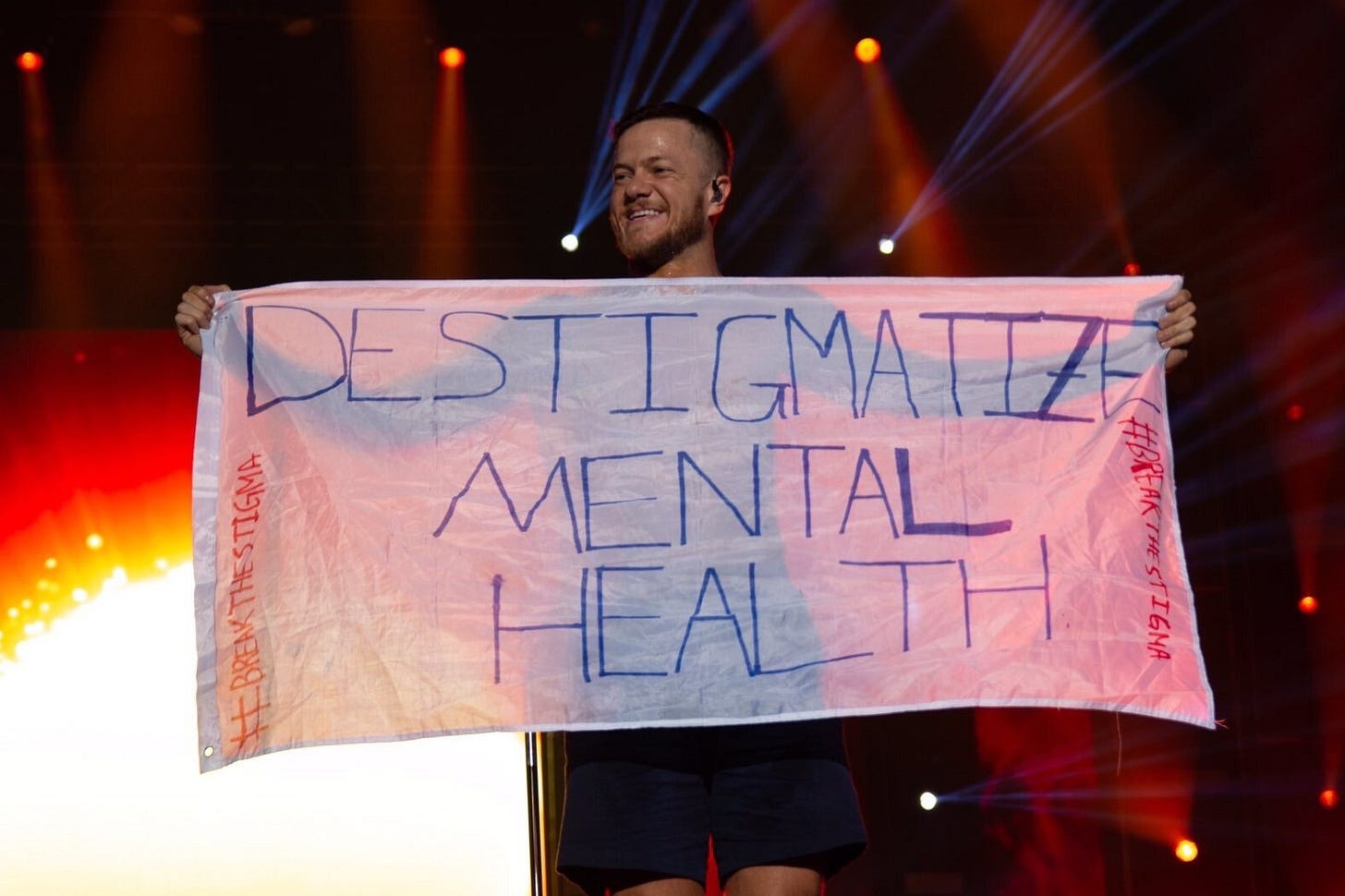 Dan Reynolds, vocalista do Imagine Dragons, segurando um cartaz que diz "Destigmatize mental health".