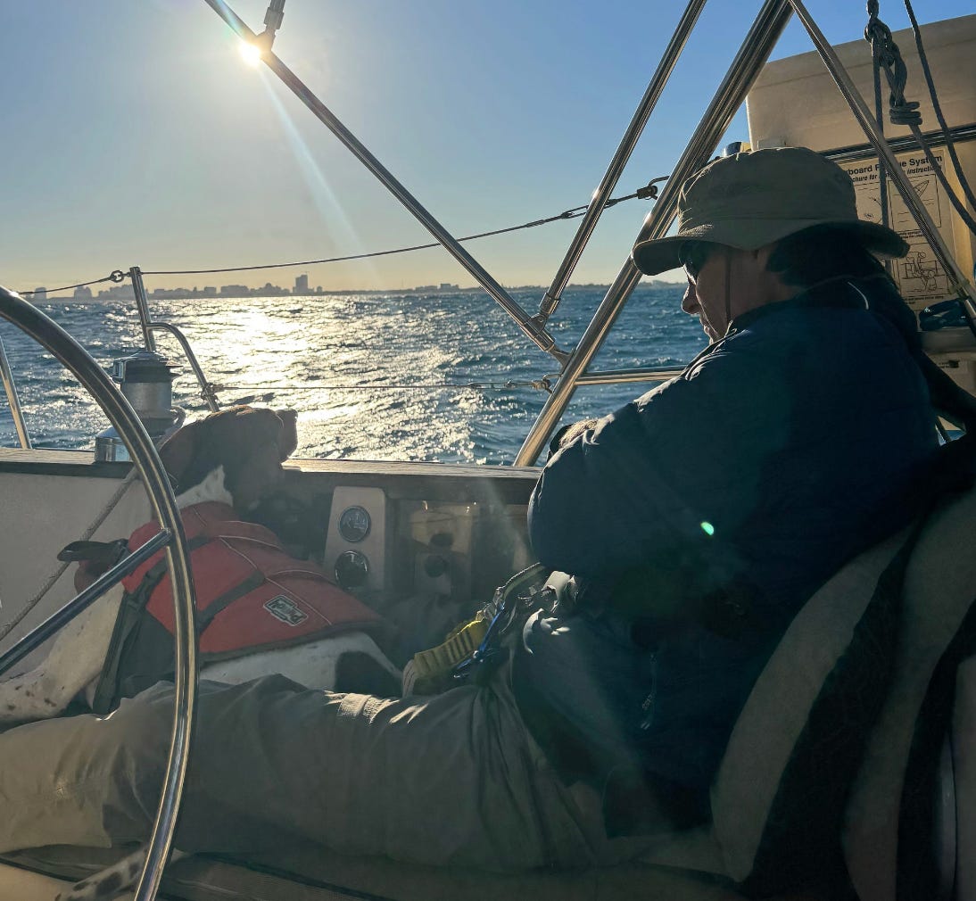 Man sits on boat, with sea behind. Beautiful shiny blue ocean and blue sky.