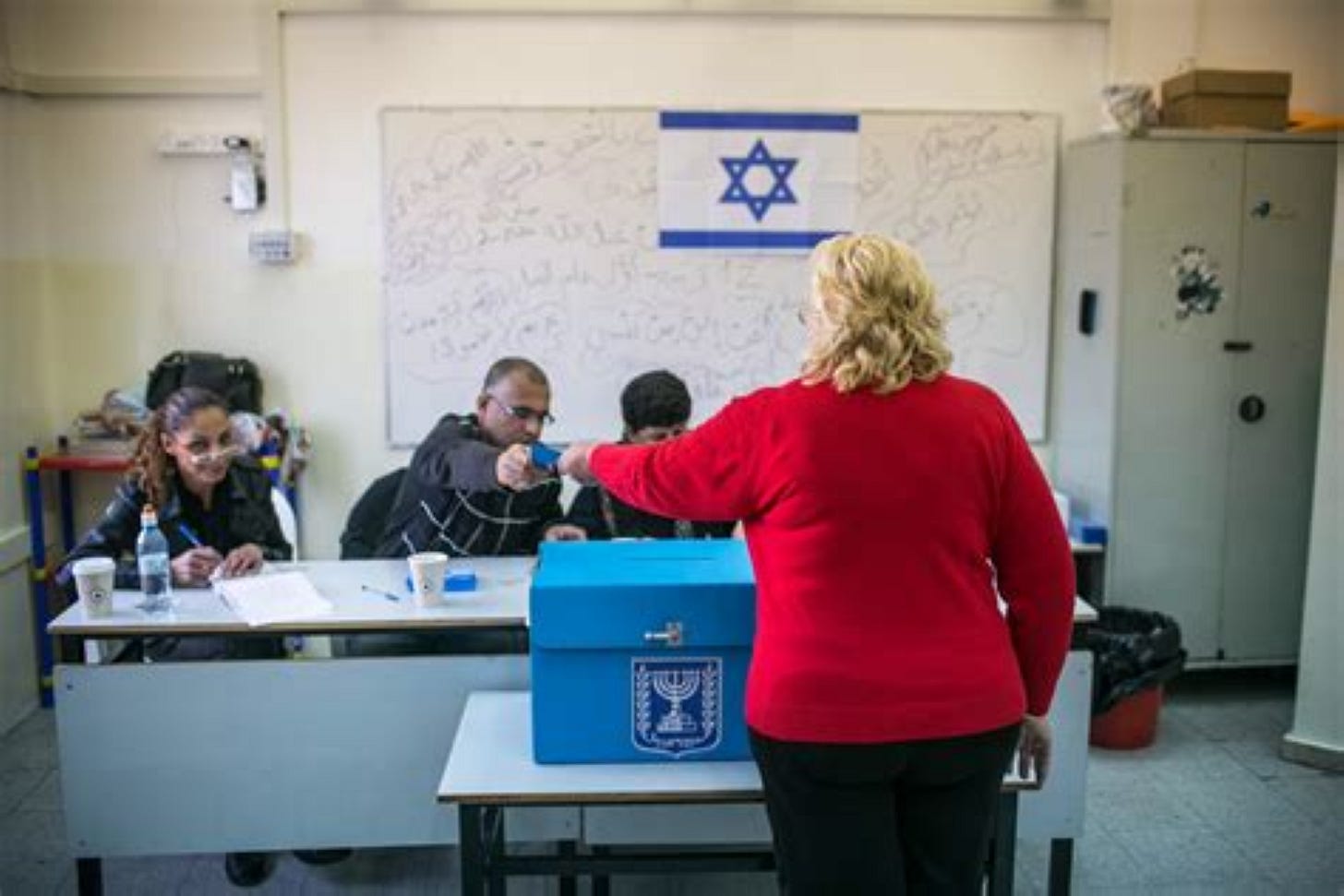Israeli poll worker handing ID card back after voter put ballot in box.