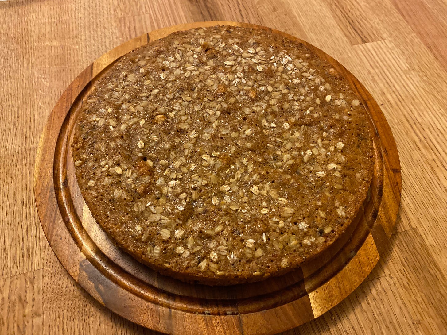 A round cake topped with oats and coarse sugar sits on a wooden plate on my kitchen counter.