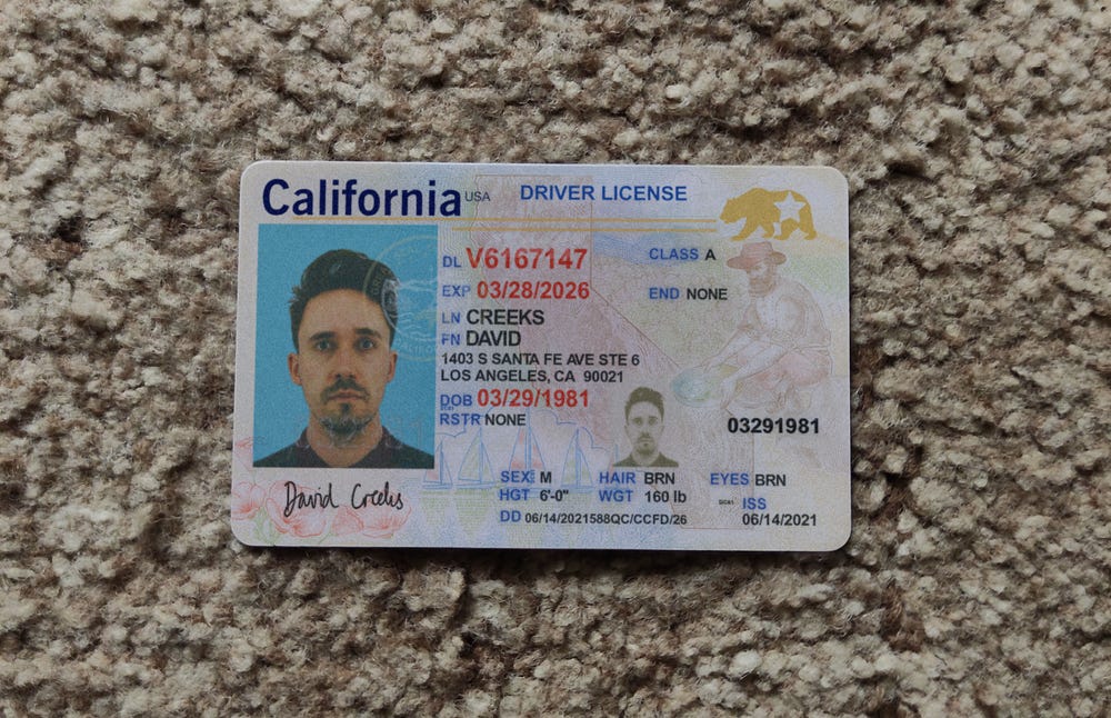 A realistic-looking California drivers license for a white man with brown hair named David Creeks sitting on a brown carpet. 