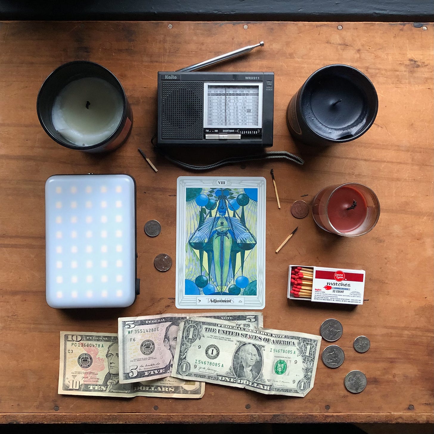 Hurricane Helene Asheville survival items: Candles, matches, radio, power bank, and money with the Adjustment tarot card from The Thoth Tarot.