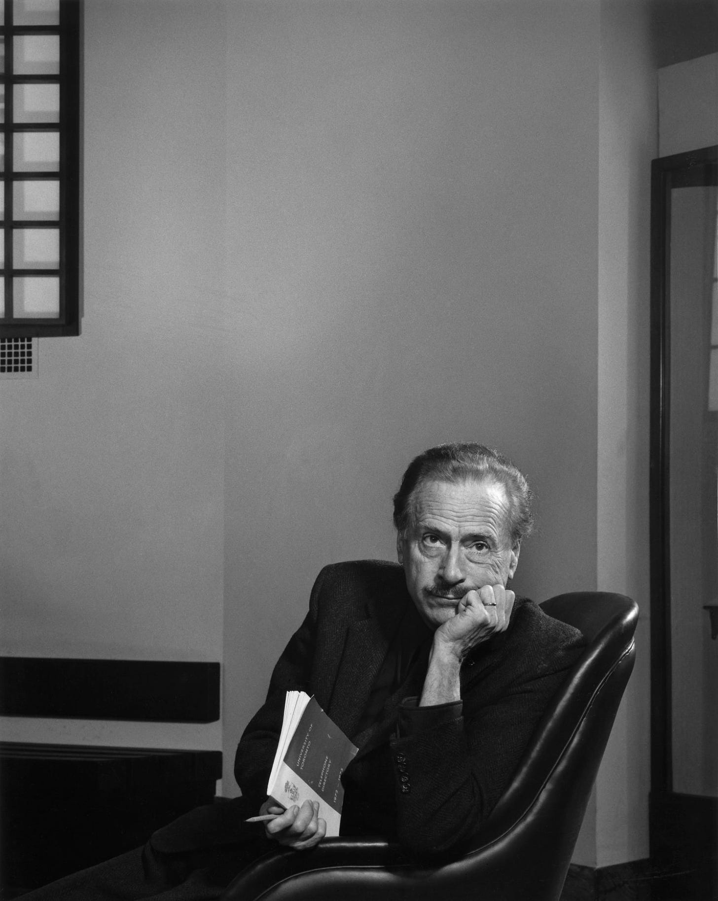 McLuhan sitting in a chair, holding a book.