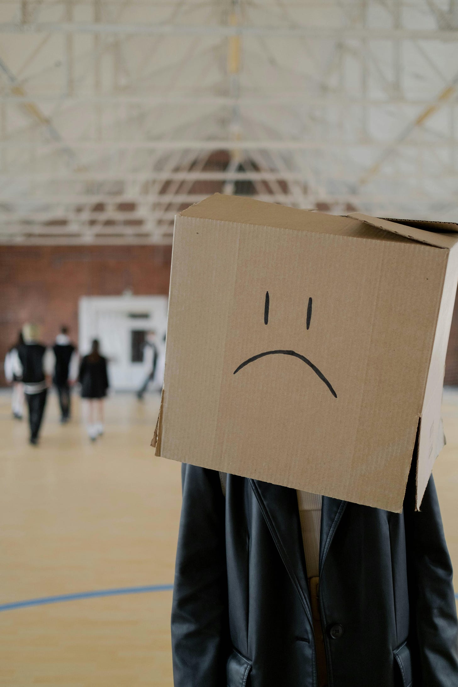 A person wearing a box on their head that has a frown drawn on it.