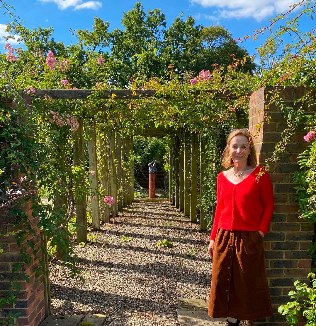 a woman in a red jumper standing by roses in a garden