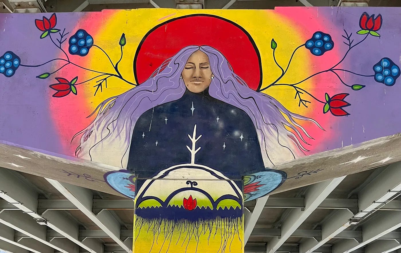 Mural of a woman with purple hair with her eyes closed. Flowers are stemming out from her body and the sun rises behind her. 