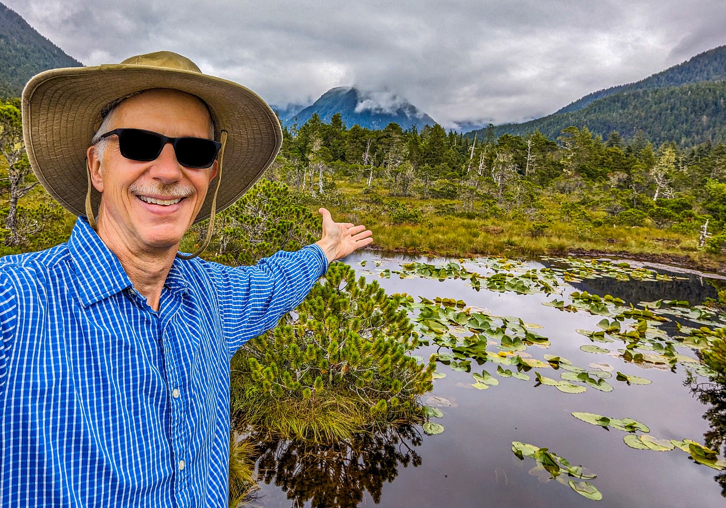 Michael standing in front of a wetland, the mountains of Alaska behind him. 