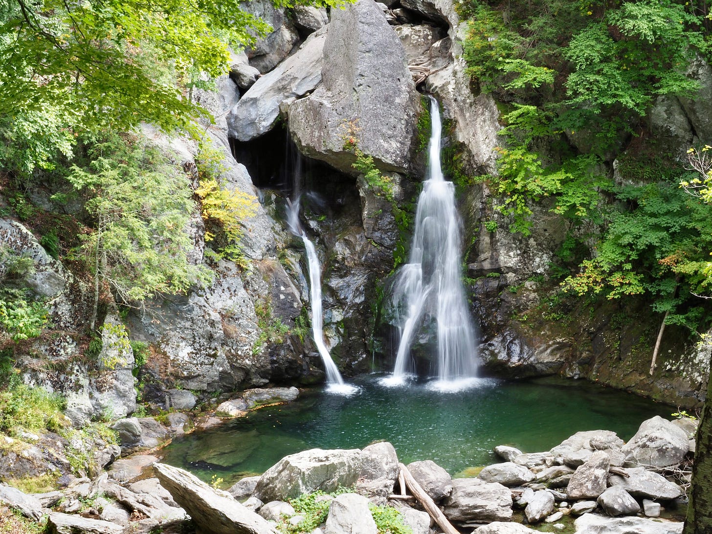 three narrow waterfalls spill into a green blue pool surrounded by rocks and green foliage