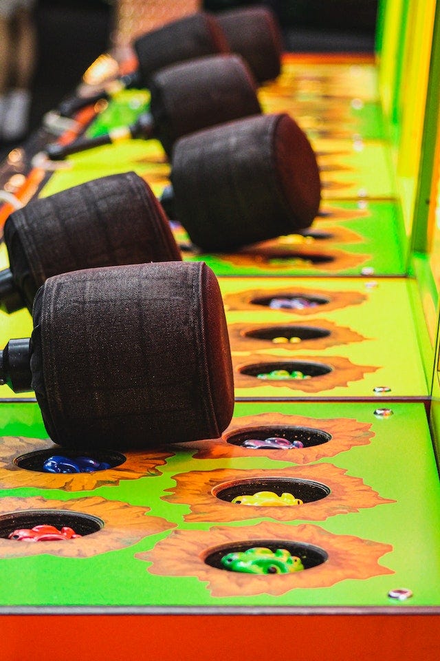 A row of yellow and orange whack-a-mole machines leading away form the camera, each with their mallet resting atop the surface.