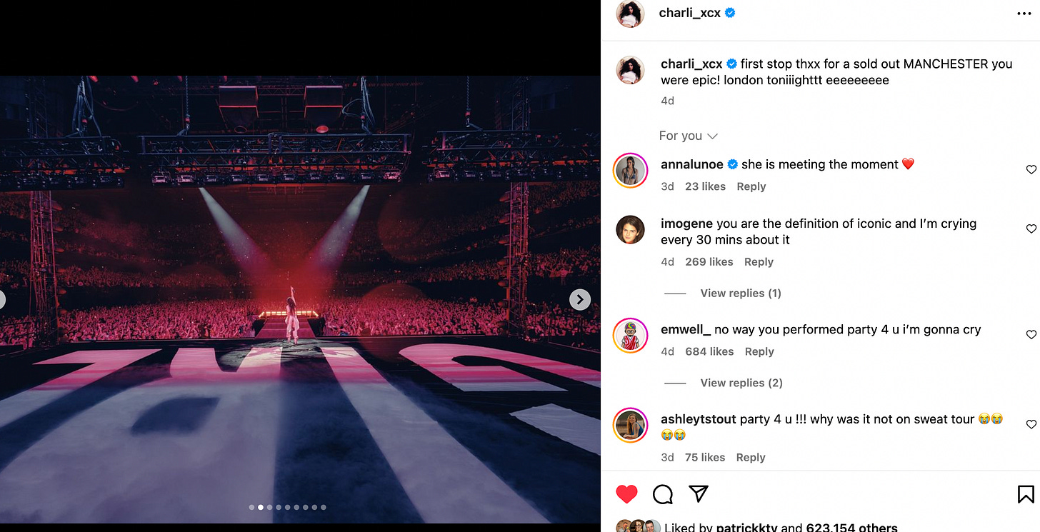 A screengrab from Charli's Insta page. With her back to the camera, Charli faces the sold out crowd, her hand up in the air. Spotlights shine on her, also showing the gigantic white letters spelling GIRL on the black floor