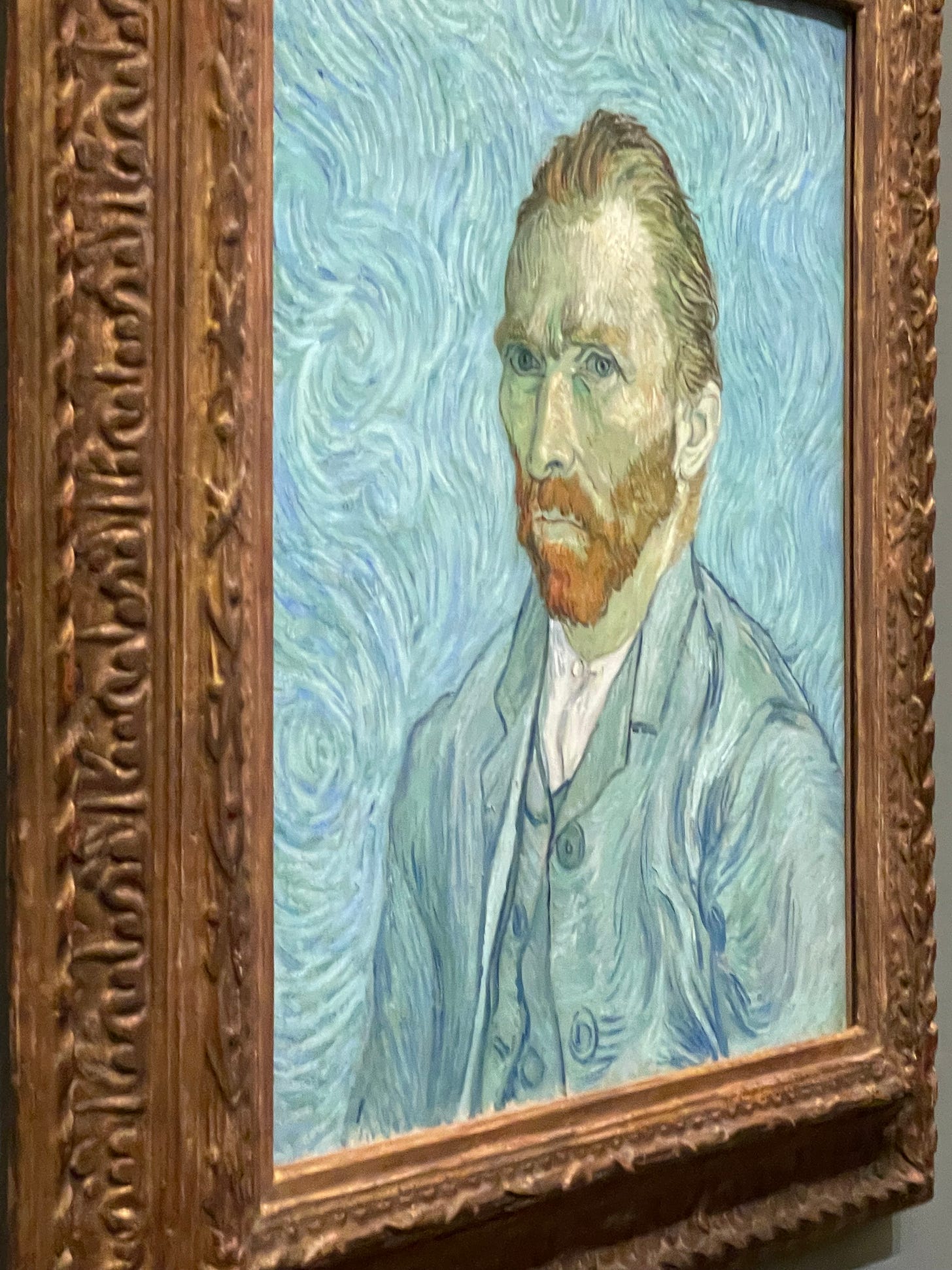 A very sharp side angle of "Portrait of the artist" by Vincent Van Gogh. The background is all blue and yellow and greens swirling into nothing. The foreground is Vincent looking stern, but thinking that he looks 'better than before'. His ginger hair and beard stand in stark contrast to the rest of the painting.
