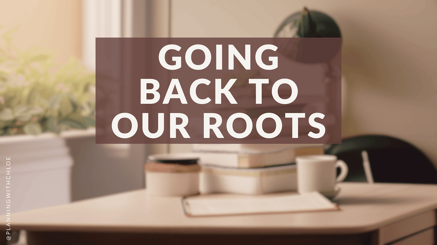 "Going back to our roots". IMG: a desk with a stack of books, a mug and plants on a window sill in the background.