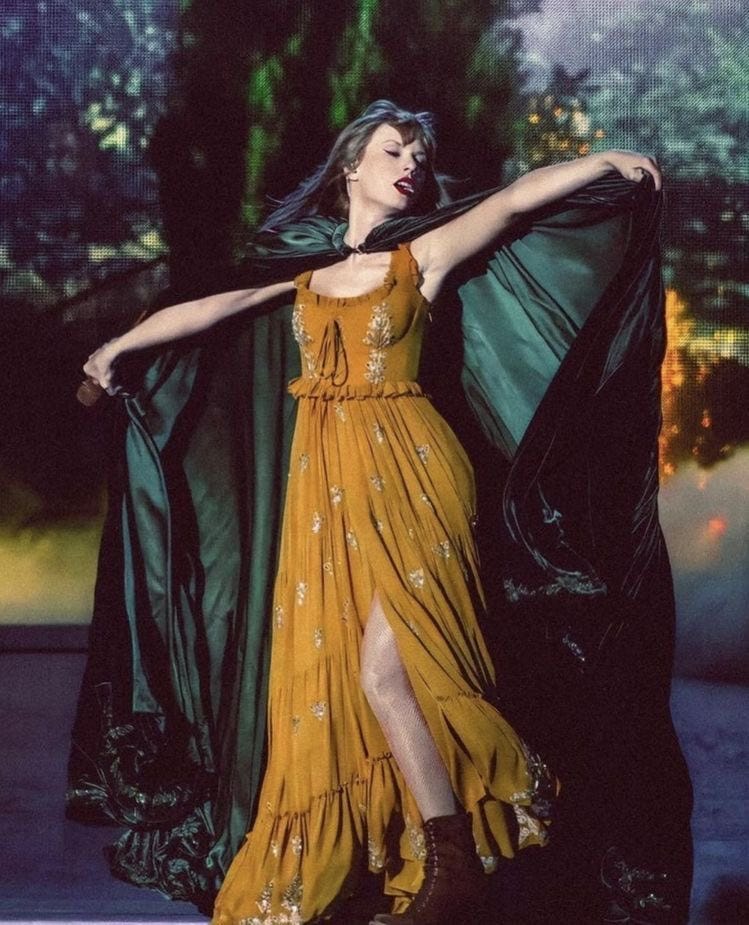 Taylor's Evermore costume - a golden yellow peasant dress and a dark green cape