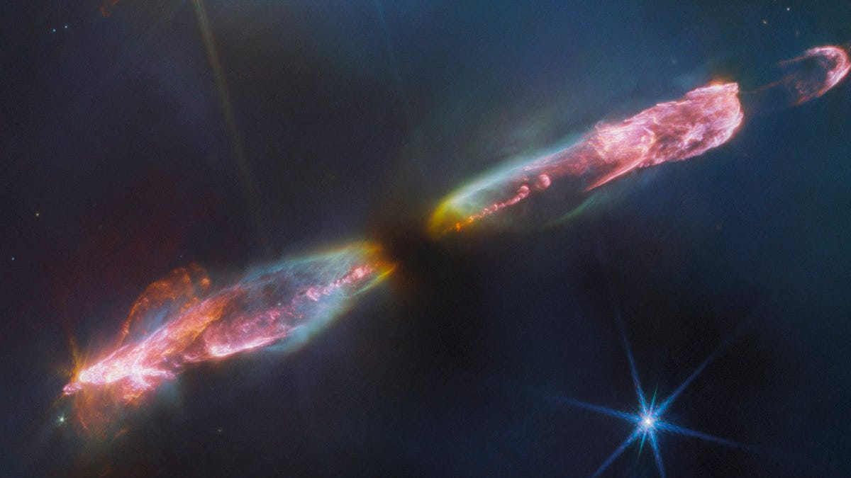 At the center is a thin horizontal pinkish cloud known as Herbig-Haro 211 that is uneven with rounded ends, and tilted from bottom left to top right. It takes up about two-thirds of the length of this angle, but is thinner and longer at the opposite angle. At its center is a dark spot. On either side of the dark spot, there are orangish yellow wisps that extend to light blue wisps. Within the center of those clouds, a pink fluffy streak runs through each lobe. At the ends of each lobe, pink becomes the dominant color. The lobe to the left is fatter. The right lobe is thinner, and ends in a smaller pink semi-circle. Just off the edge of this lobe is a slightly smaller pink semicircle, then a pink sponge-like blog. The background contains several bright stars, each with eight diffraction spikes extending out from the central bright point.