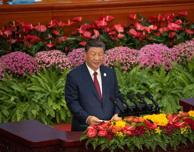 Xi Jinping surrounded by flowers as he delivers a speech.