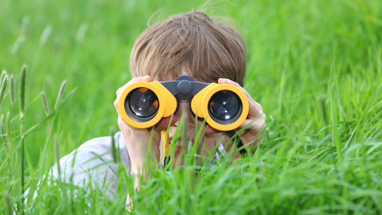 A boy in the grass using yellow binoculars. 