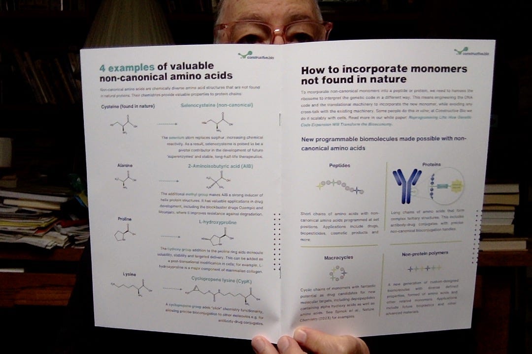 Some old bald guy peering from behind a two-page glossy handout explaining how construcitive.bio is reinventing the genetic code. Some old bald guy peering from behind a two-page glossy handout explaining how construcitive.bio is reinventing the genetic code.