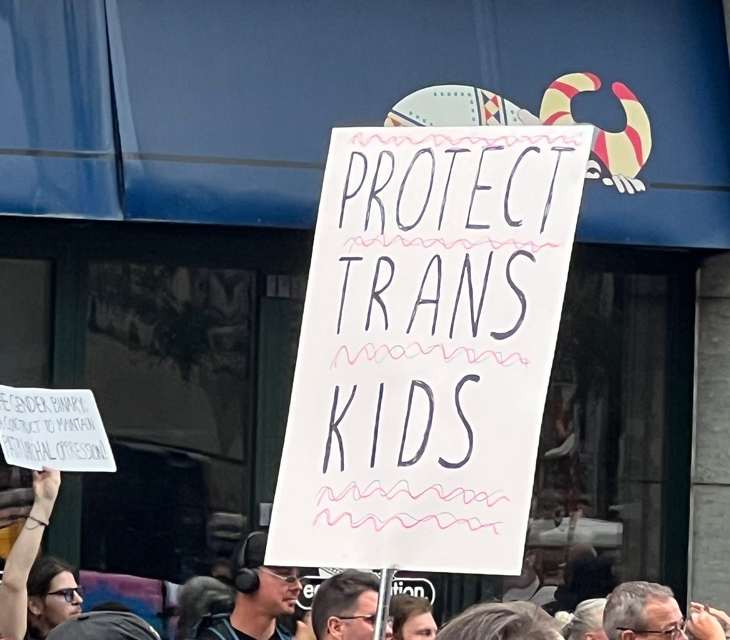 A marcher holds a sign that says Protect Trans Kids.