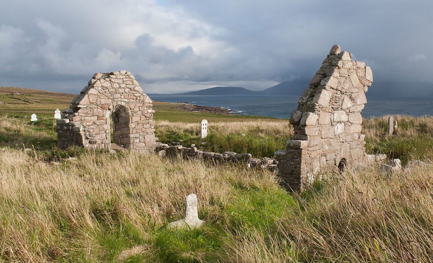 Photo showing the remains of a twelfth-century stone church adjacent to a body of water, with hills visible in the distance.