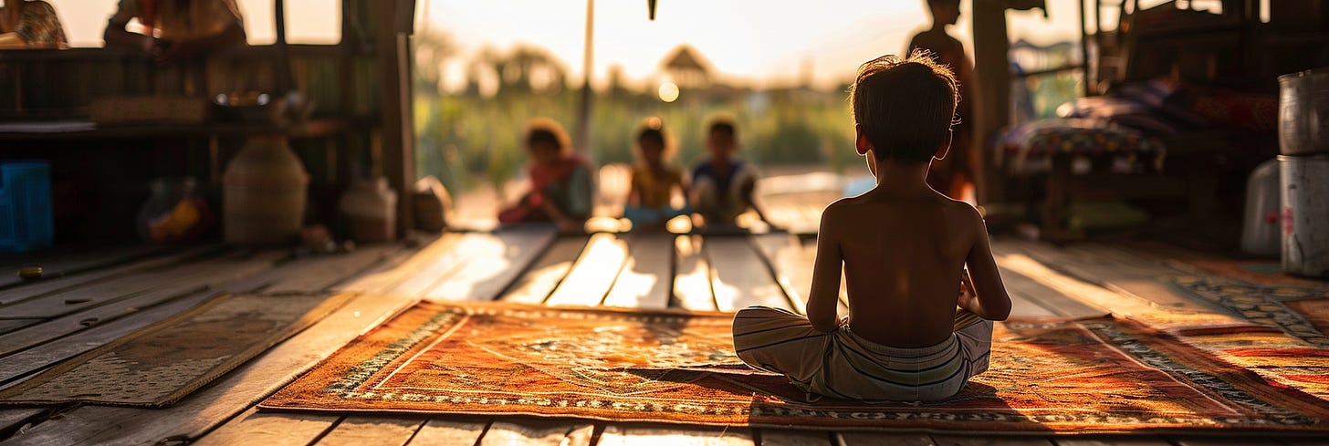 A child sits cross-legged on a vibrant, patterned rug, facing away from the camera in an open, rustic setting. The background is softly blurred, with other children sitting in the distance and warm sunlight streaming through, creating a peaceful atmosphere.