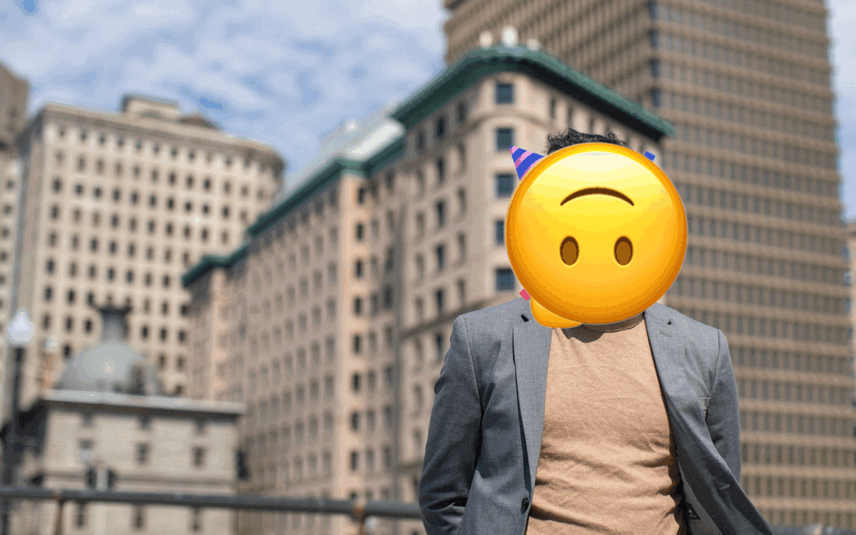 A series of emojis cycles through the place where Abdullah's head is supposed to be. In the background the Providence skyline can be seen. Abdullah is wearing a brown turtleneck and a grey blazer.