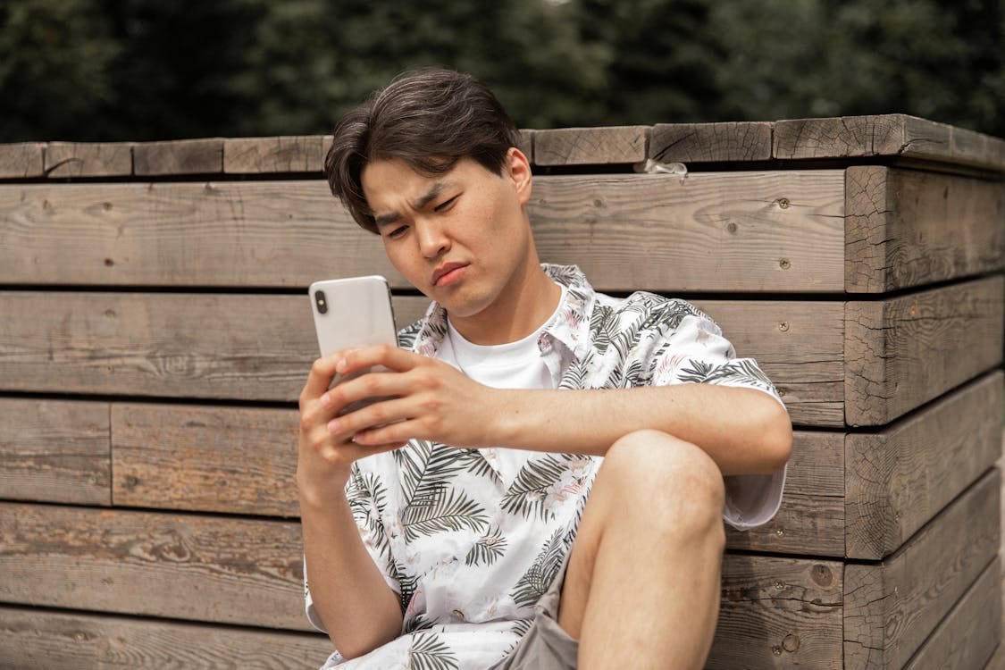 Free Asian displeased man browsing smartphone in countryside Stock Photo