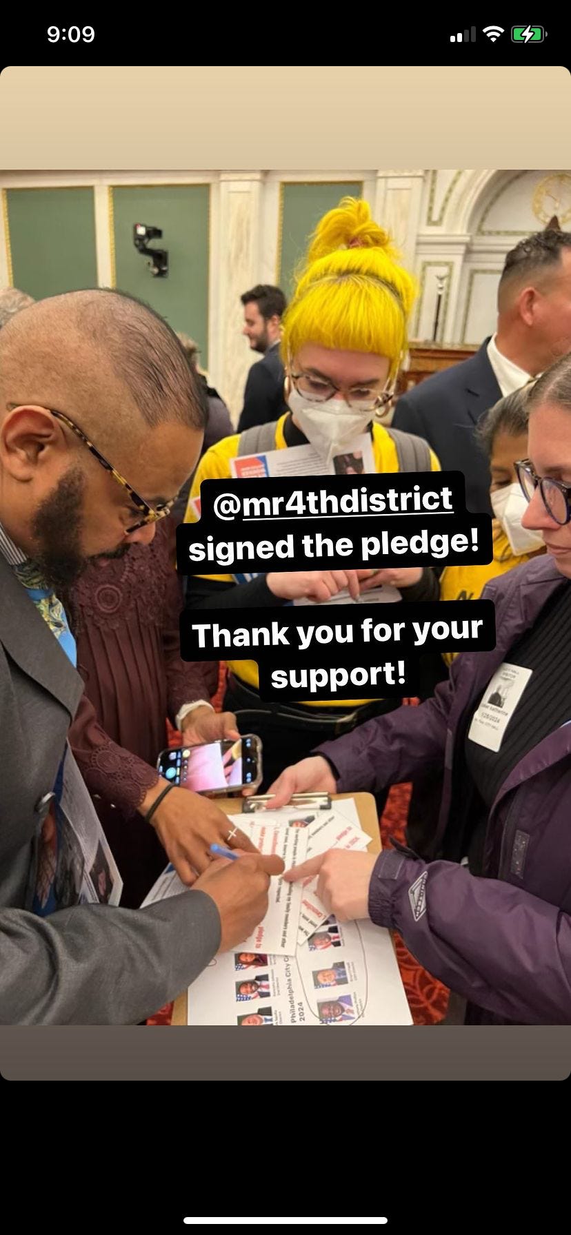 Worker holding a physical pledge out and a city council member is signing it.