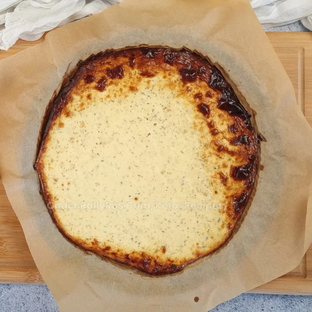 A freshly baked cottage cheese pizza on parchment paper, with a golden-brown crust and a creamy white cheese topping that is slightly browned in spots, indicating it has been baked to perfection.