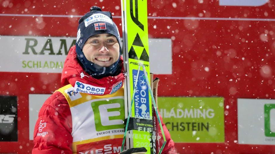 Jarl Magnus Riiber holding skis and smiling as snow falls