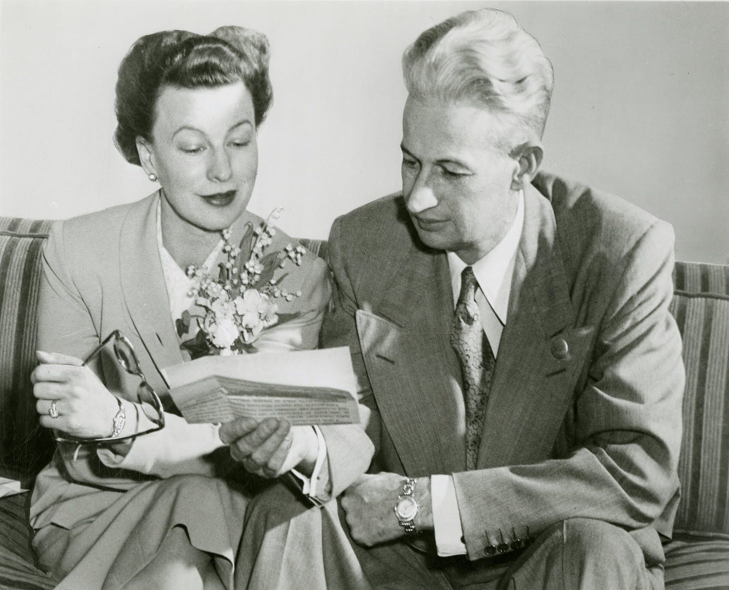 Black & white photo of a woman and a man, both in dressed in suits, looking over a document (1950)