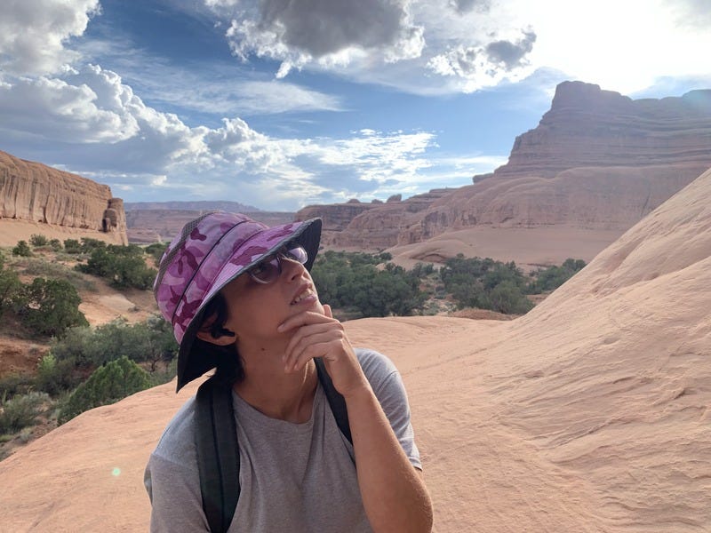 Rey in a wide sandstone canyon, looking up with a thoughtful expression