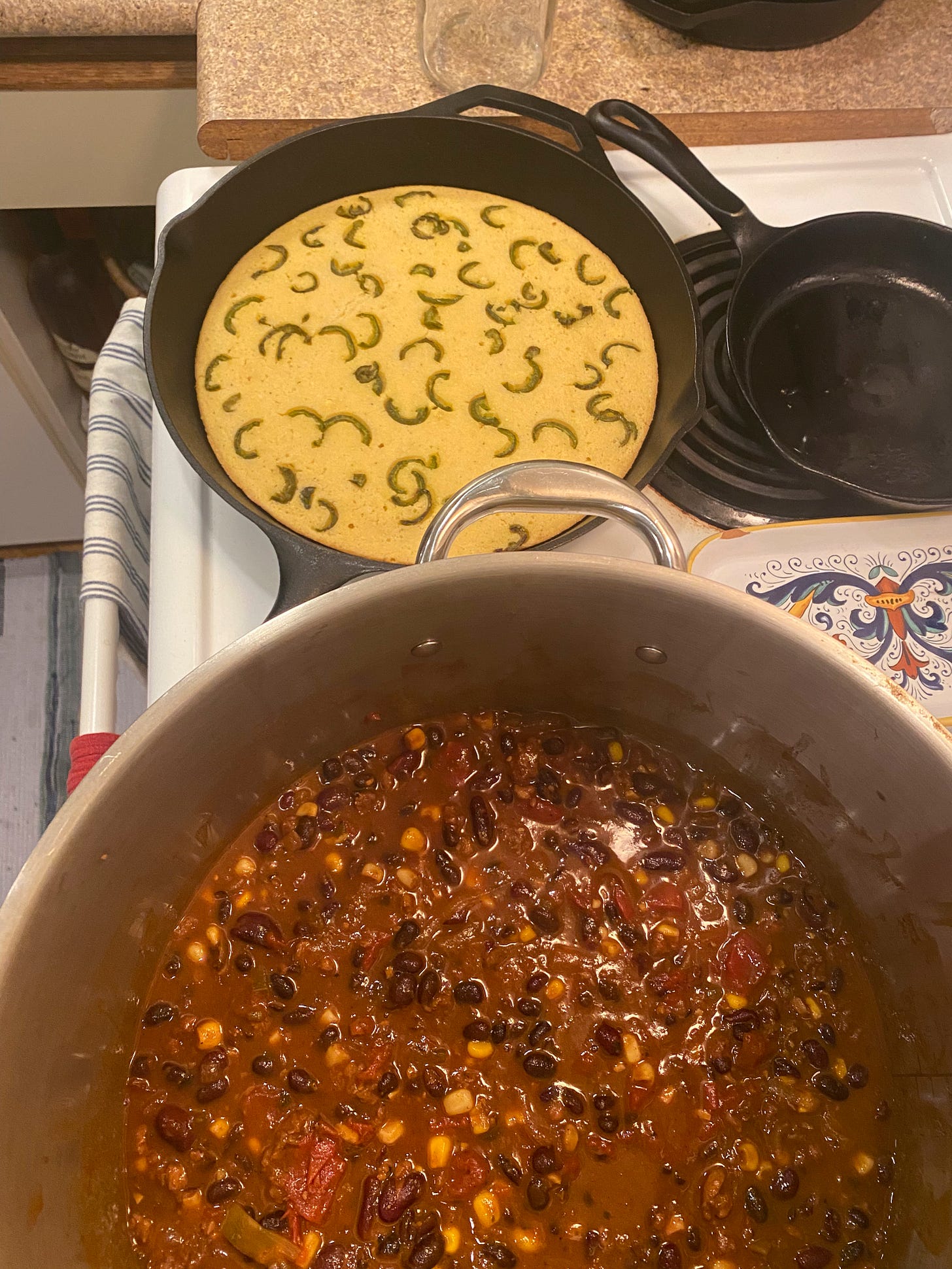 On the stove is a cast iron pan of cornbread with slices of jalapeño baked in. In front of it is a large stockpot, with the chili described above in it.