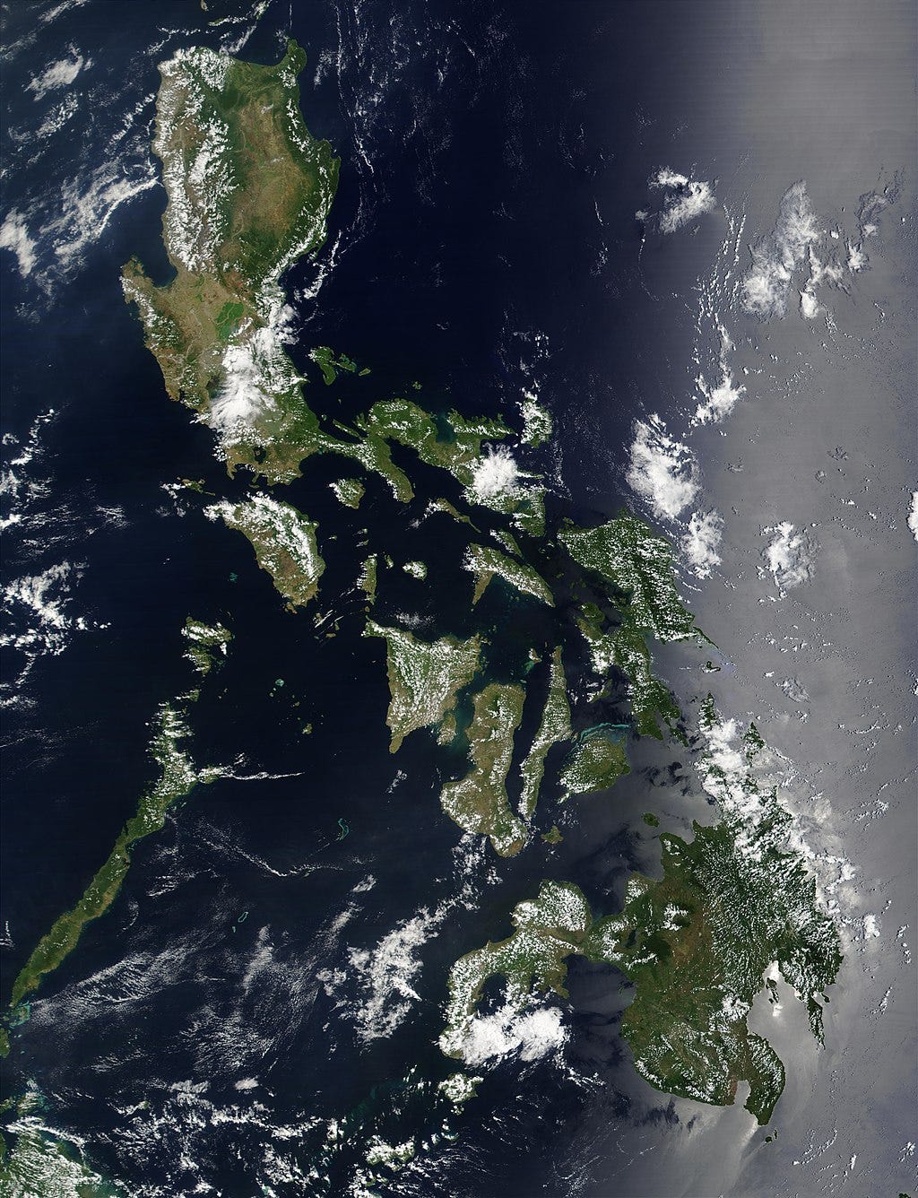 satellite image of the Philippines, there are clouds covering some of the islands which appear brown and green. the ocean is dark blue