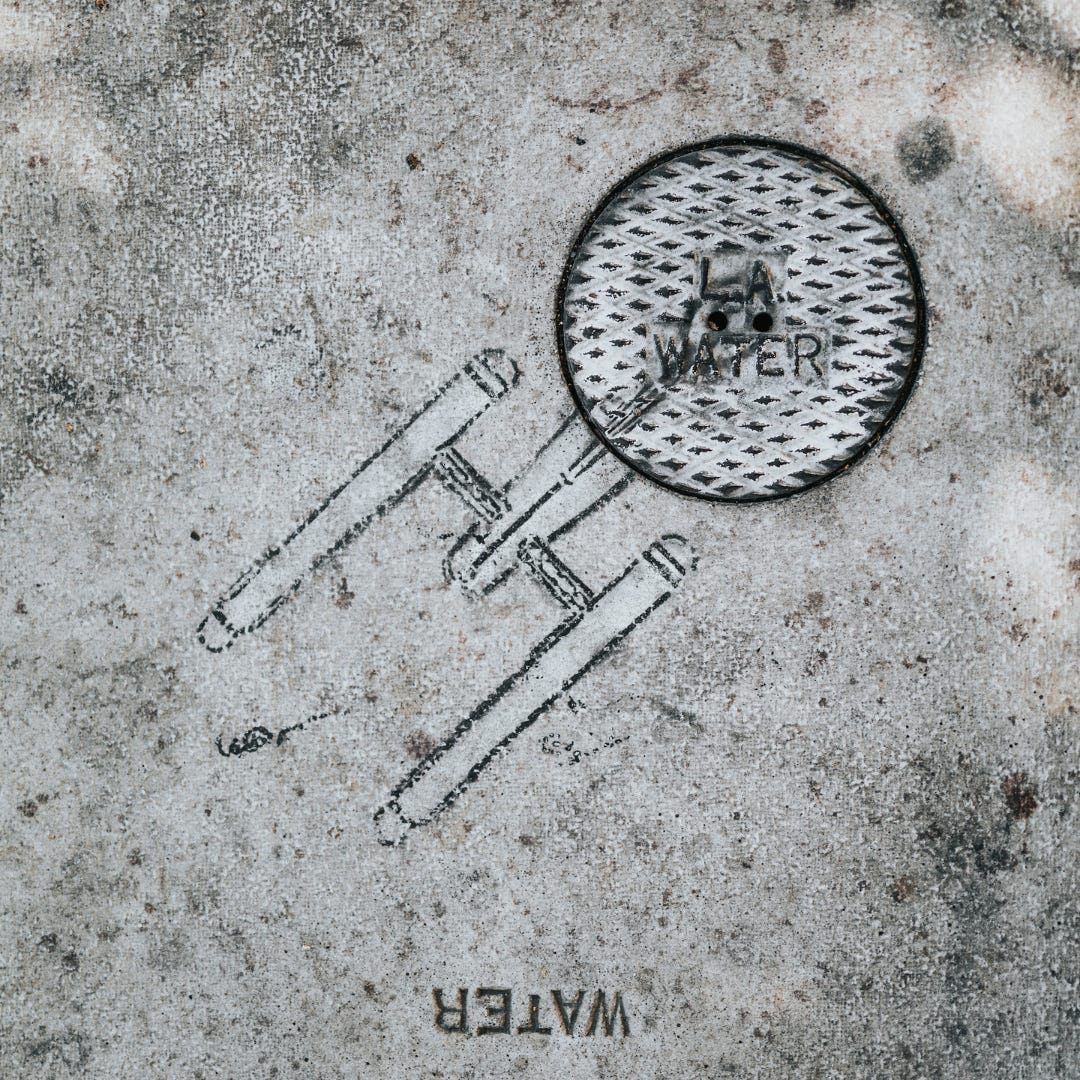 An image of the Starship Enterprise is etched into a city side walk. A manhole cover with the word “water” is used to create the front disk portion of the spaceship