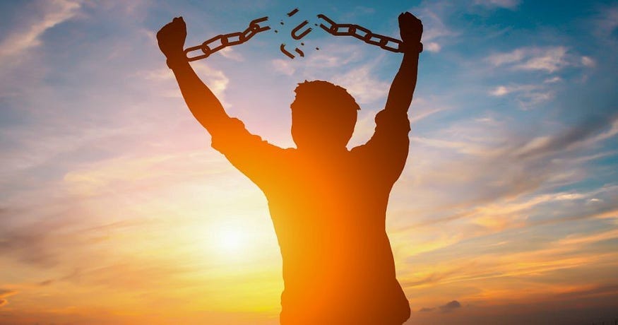 A shadowy photo of a man breaking his shackles with the sun and the sky in the background.