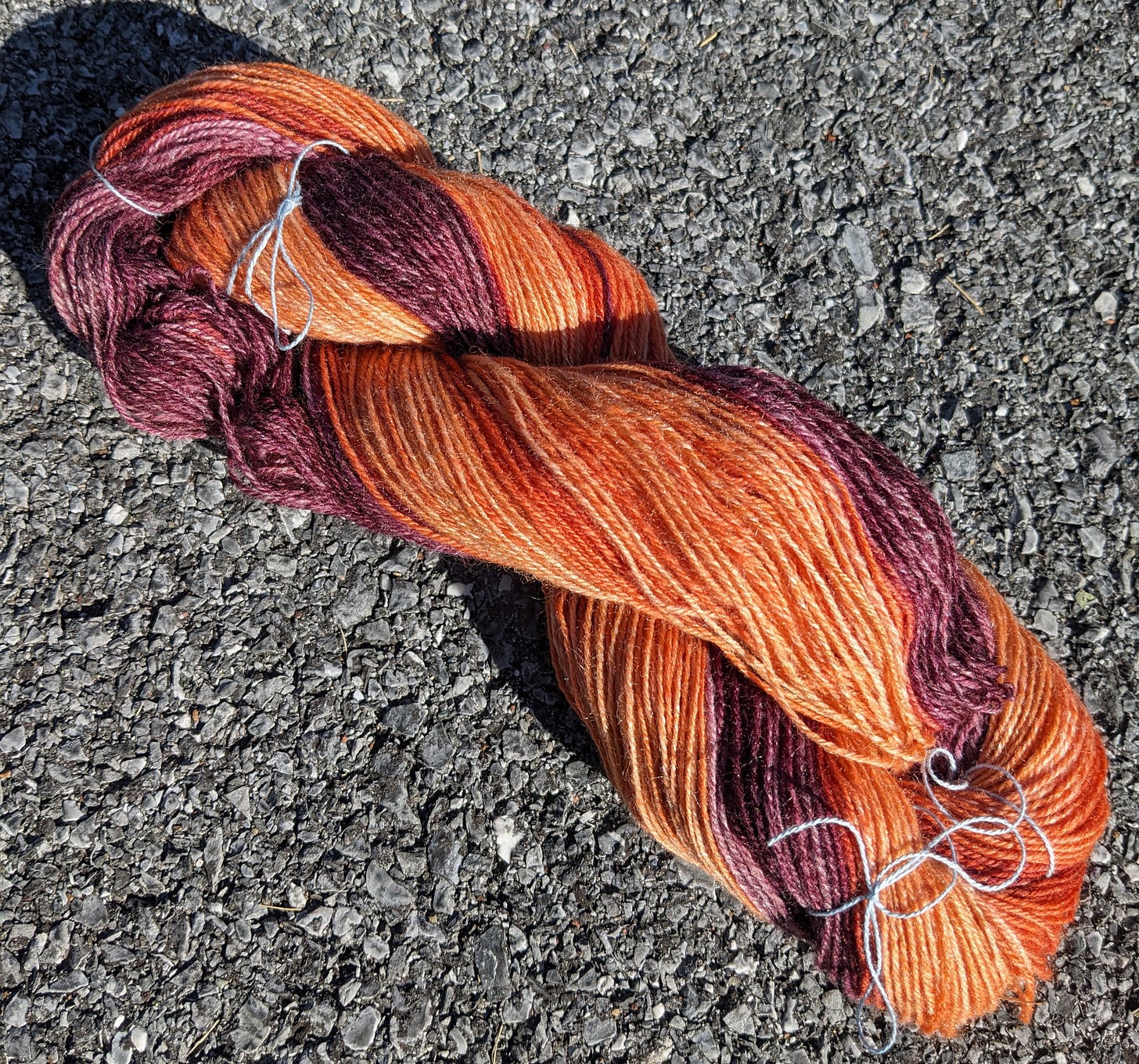 A photograph of a skein of yarn that fades from a bright peachy orange to a deep red-purple