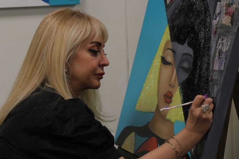 A woman with blonde hair paints on a canvas.