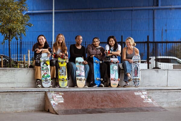 Six women sitting together are all holding skateboards.