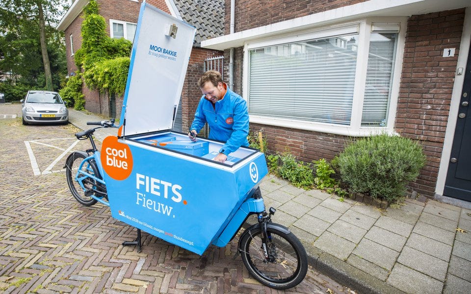 A cycling courier unloads a package from the box on his cargobike whilst parked outside a house on a dutch residential street. 